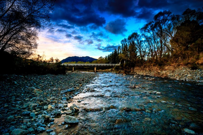 River flowing under a bridge at dusk with mountains