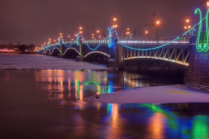 Bridge decorated with lights over a river in winter at night