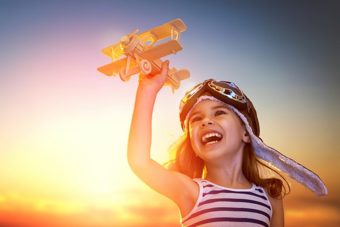 Girl in pilot helmet holding toy airplane