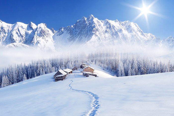Winter mountain landscape with wooden cabins and sun rays
