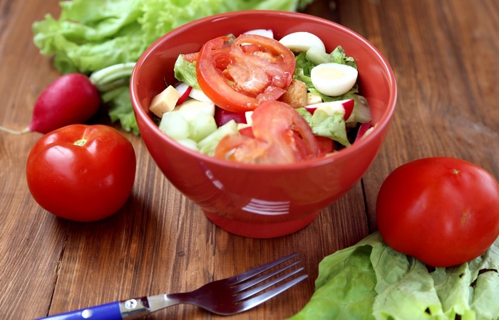 Salad with tomatoes, cucumbers, radishes, and eggs in a red bowl
