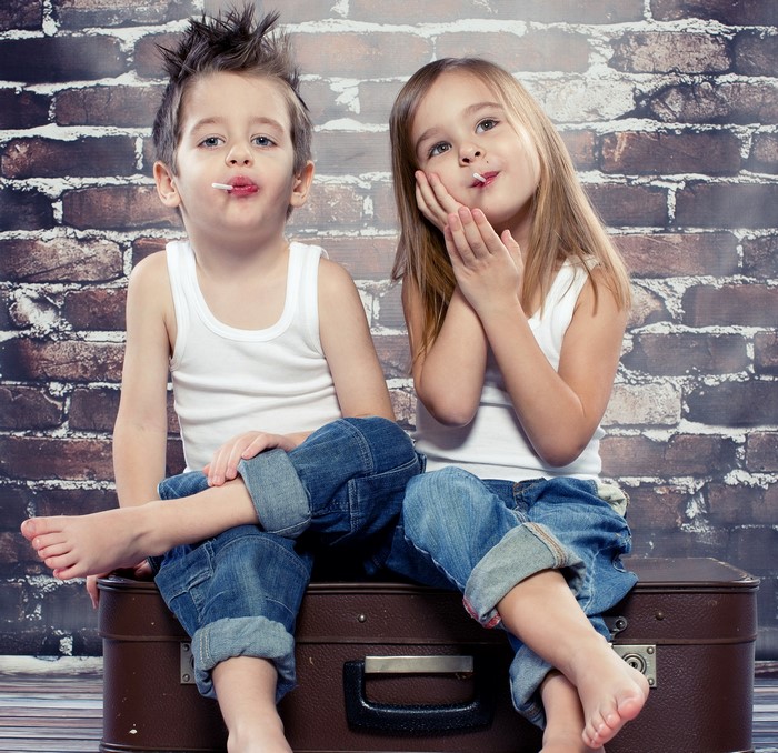 Two children with lollipops sitting on a suitcase