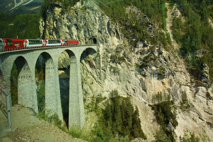 Red train on a stone viaduct in the Swiss Alps