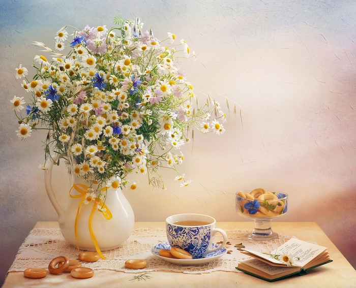 Still life with bouquet of daisies and cornflowers, tea cup, and pastries