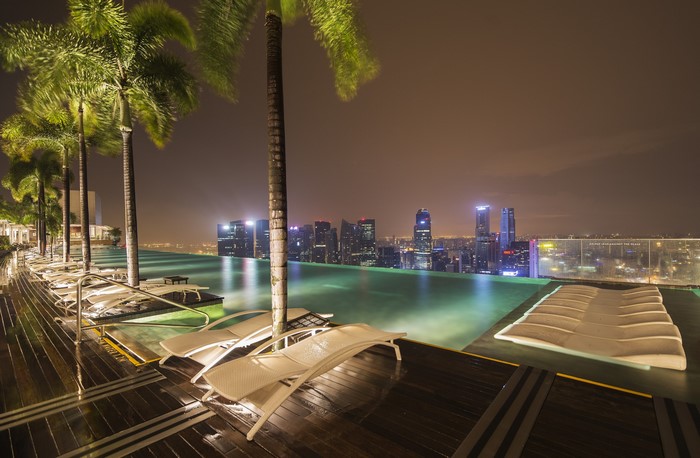 Infinity pool with palm trees and Singapore skyline at night