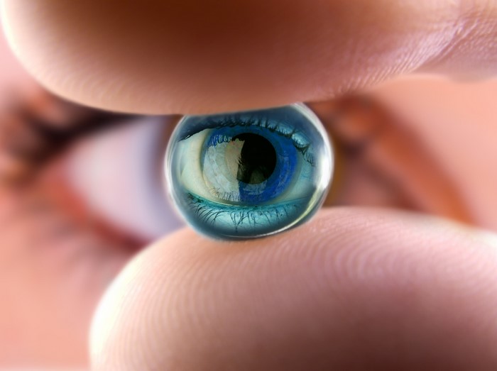 Eye reflected in a water droplet held by fingers
