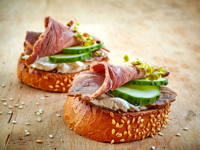 Two open-faced sandwiches with ham, cucumber, and sprouts