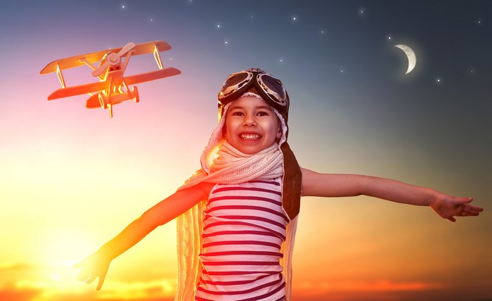 Girl in pilot costume with toy airplane at sunset