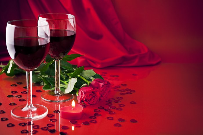 Two glasses of red wine with a rose and candle