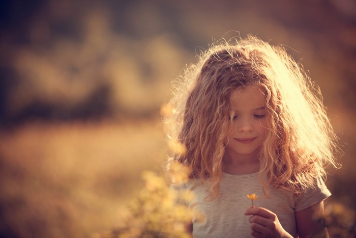 Young girl with curly hair holding a flower