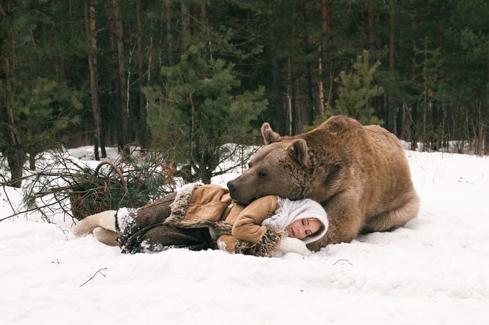 Woman sleeping with a brown bear in the snow