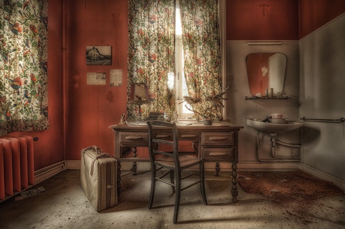Abandoned room with desk, chair, and suitcase