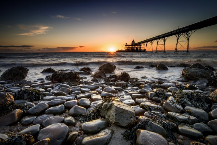Pier over the sea at sunset with rocky beach