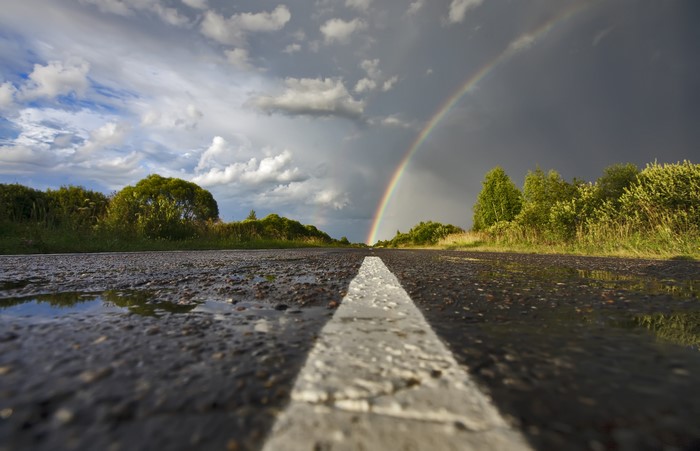 Asphalt road with rainbow and clouds