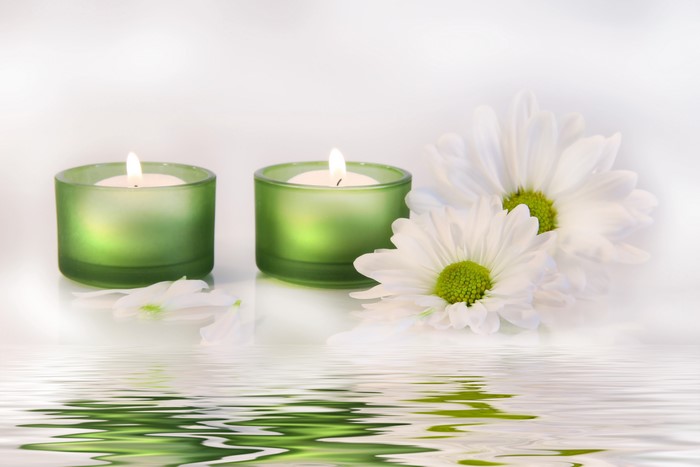 Two lit candles and white chrysanthemums reflected in water