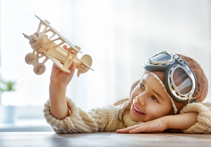 Little girl in pilot hat and goggles holding airplane