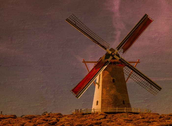 A Dutch windmill with red sails against a textured sky