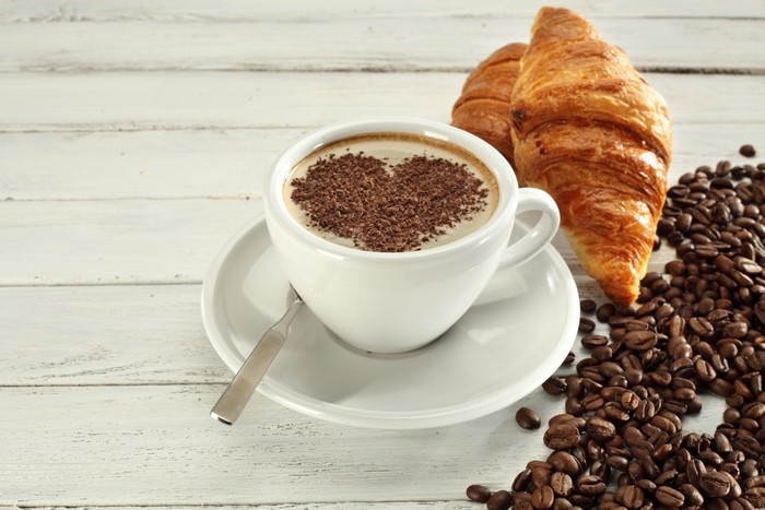 Coffee cup with heart-shaped chocolate shavings, croissants, and coffee beans