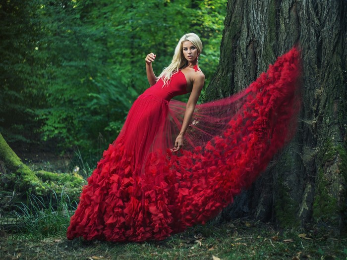 Blonde woman in red dress by tree trunk