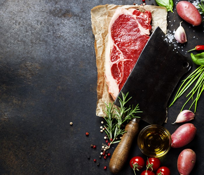 Raw steak with butcher knife and vegetables