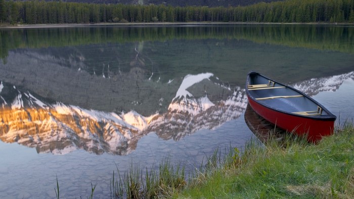Red canoe on a calm lake with mountain reflection