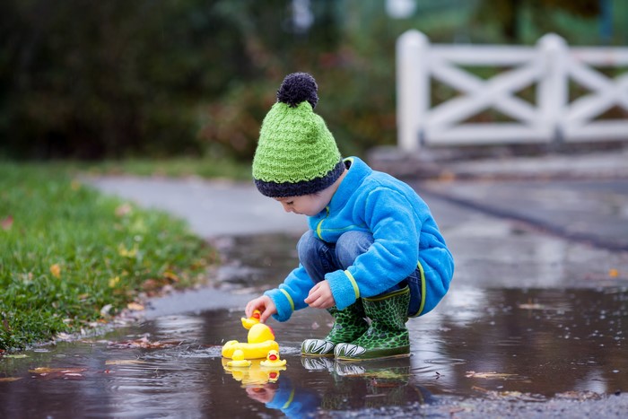 Boy in Winter Hat Playing with Rubber Ducks in Puddle