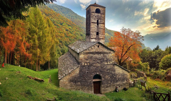Stone church with bell tower in autumn mountains, Lombardy, Italy