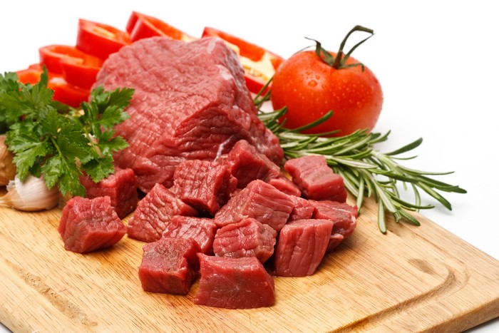 Raw beef cubes with vegetables on a cutting board