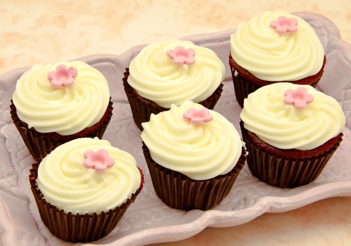 Six red velvet cupcakes with white frosting and pink flowers