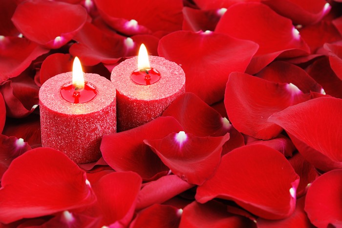 Two red candles surrounded by red rose petals