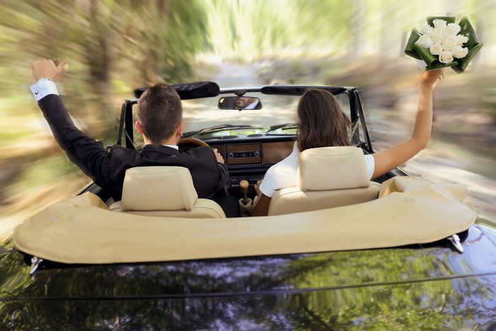 Newlyweds in a convertible with a bouquet