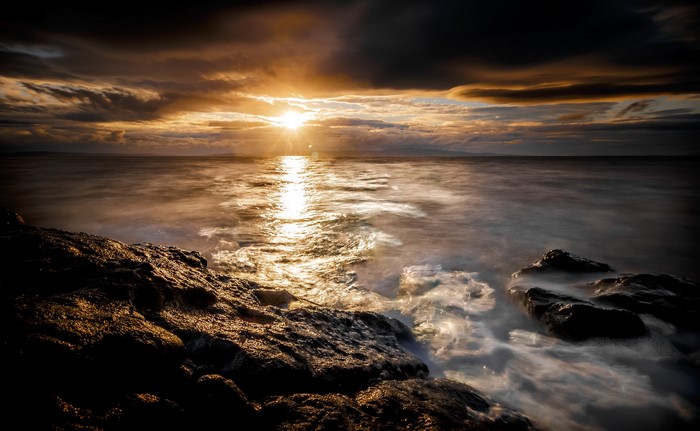 Sunset over the ocean with rocky shore