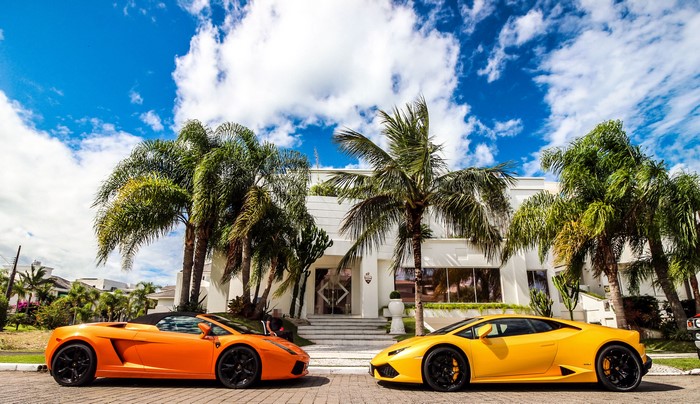 Two Lamborghinis parked in front of a modern house with palm trees