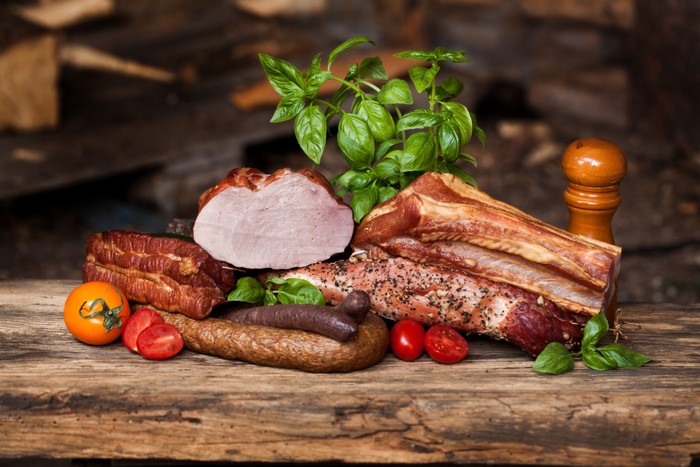 Meat products, sausage, ham, tomatoes, and foliage on a wooden table