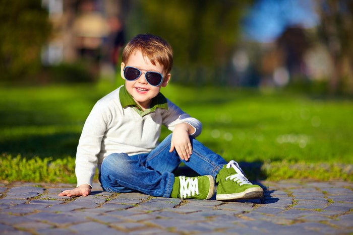 Boy in sunglasses and jeans sitting on cobblestones