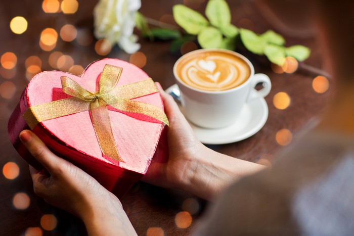 Hands holding a heart-shaped gift box with a cup of coffee
