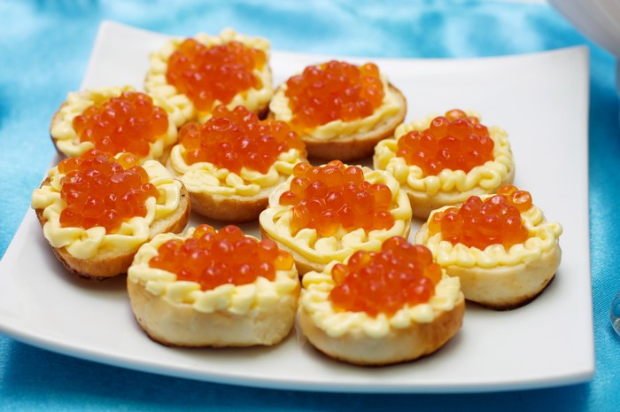 Appetizers with red caviar and cream on a white plate