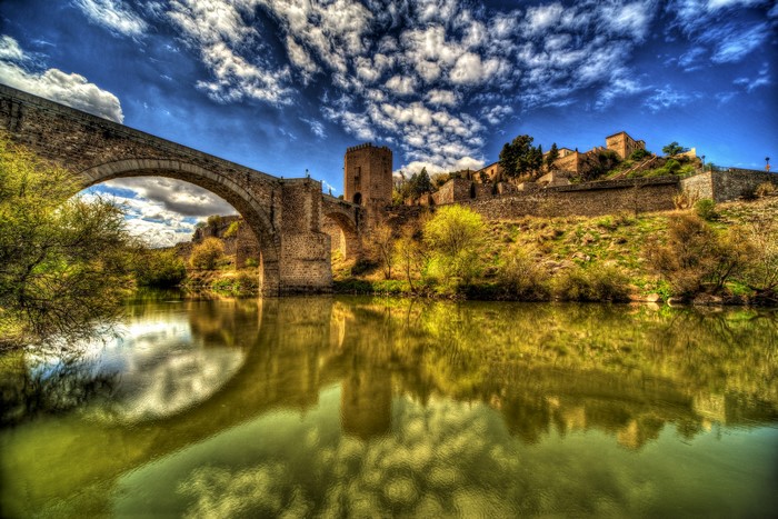 Stone bridge over a river with a castle on a hill in Toledo, Spain