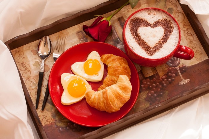 Breakfast tray with heart-shaped eggs, croissants, and cappuccino