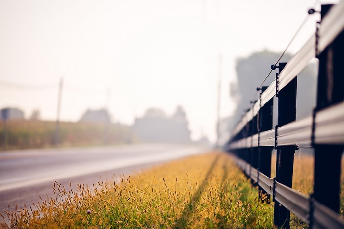 Roadside fence with grass and a foggy road