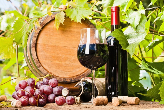 Red wine bottle, glass, grapes, and barrel