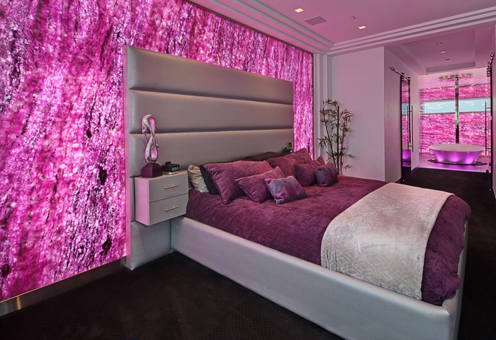 Bedroom with purple bedding and pink illuminated wall
