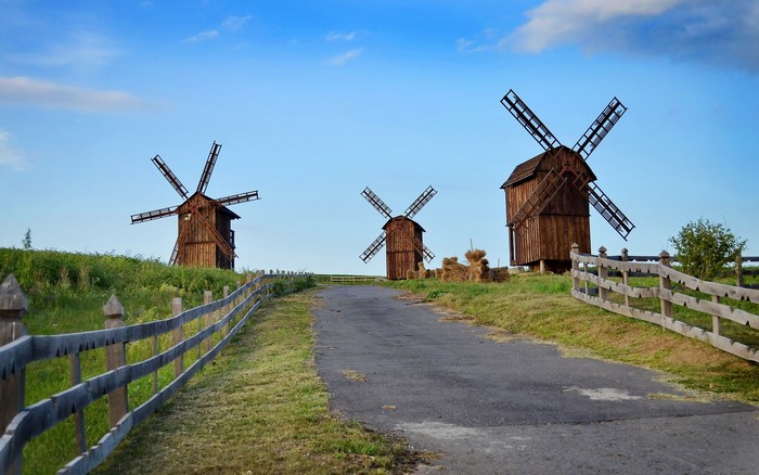 Three wooden windmills on a grassy hill under a blue sky