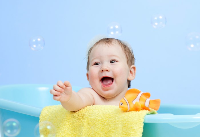 Baby in bathtub with toy fish and bubbles