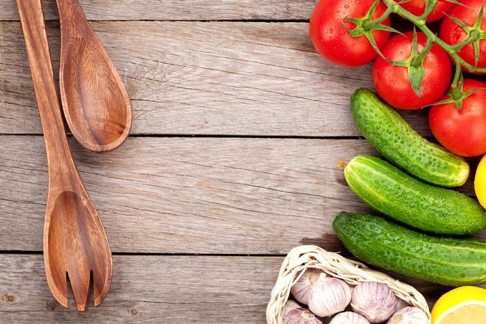 Tomatoes, cucumbers, garlic, and wooden spoons on wood planks