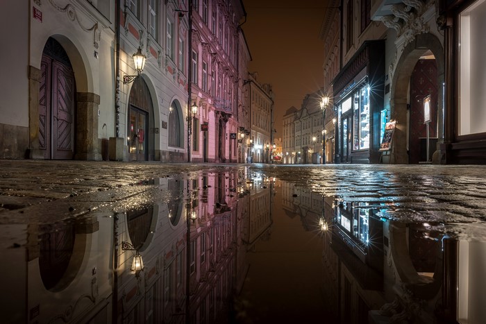 Cobblestone street with puddles reflecting buildings at night