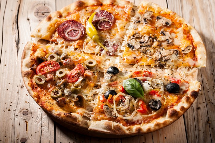 Four-section pizza with various toppings on a wooden table
