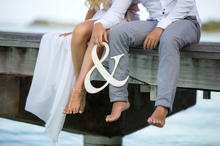 Couple sitting on a dock holding an ampersand