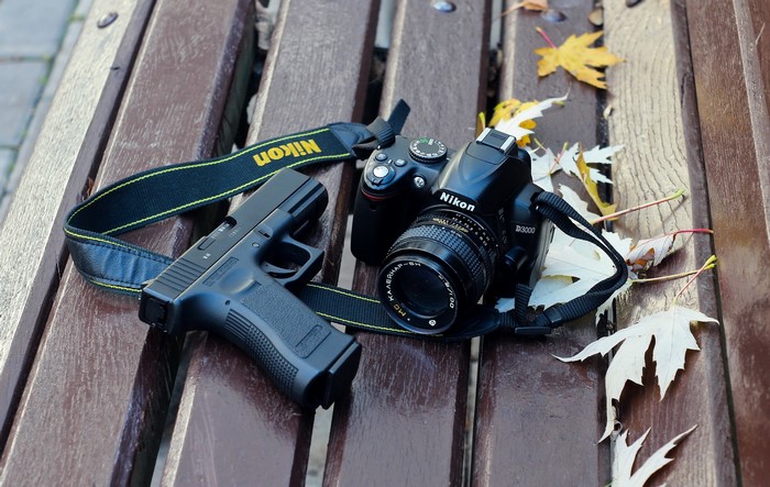 Nikon D3000 camera and pistol on a wooden bench