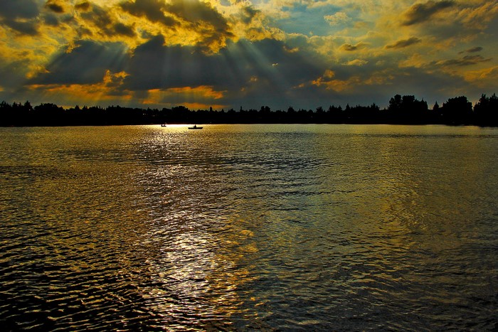 Sunset over a river with boats and silhouetted trees